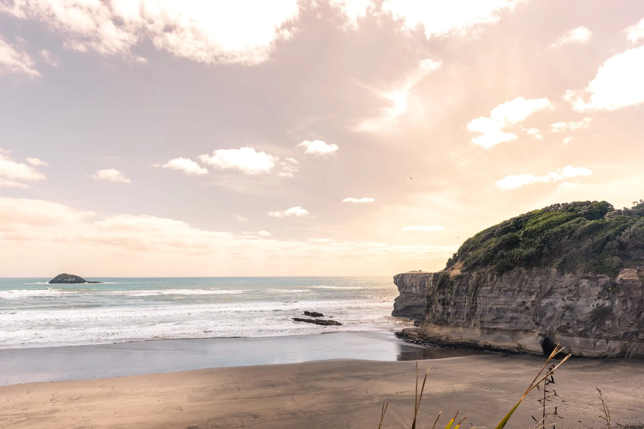 Sunset over a sandy beach and rocky headland on New Zealand's west coast
