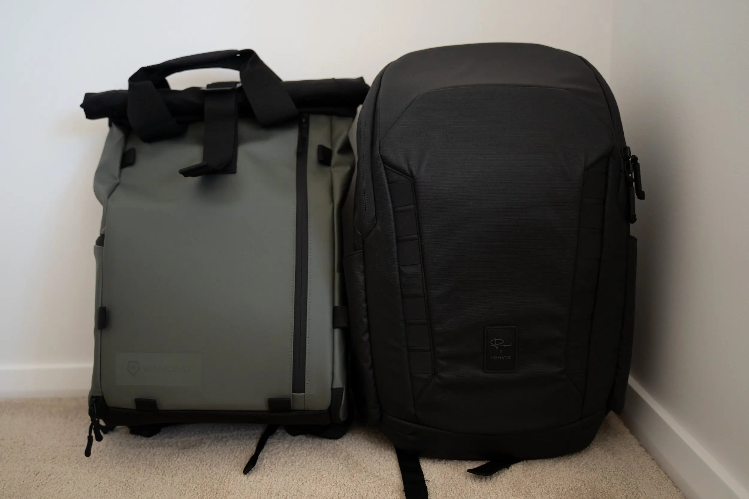 Wandrd PRVKE Lite backpack in green beside a larger black camera backpack