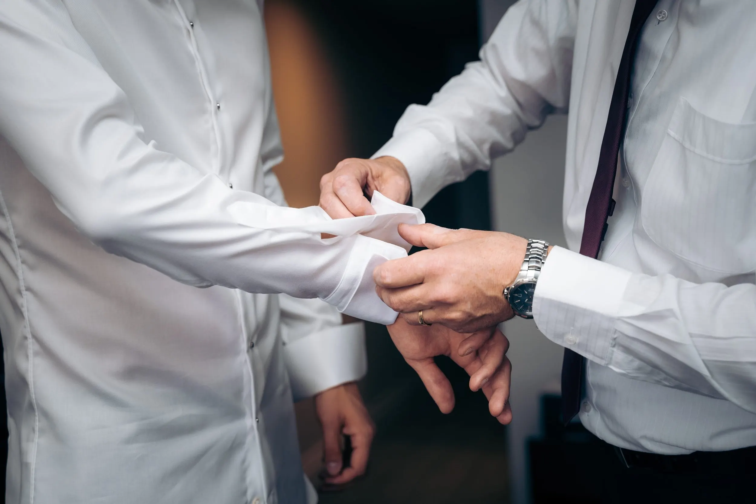 Two people, one in a white shirt with a watch, helping the other in a white lab coat with cuffed sleeves, adjust a medical sleeve or band on their arm.