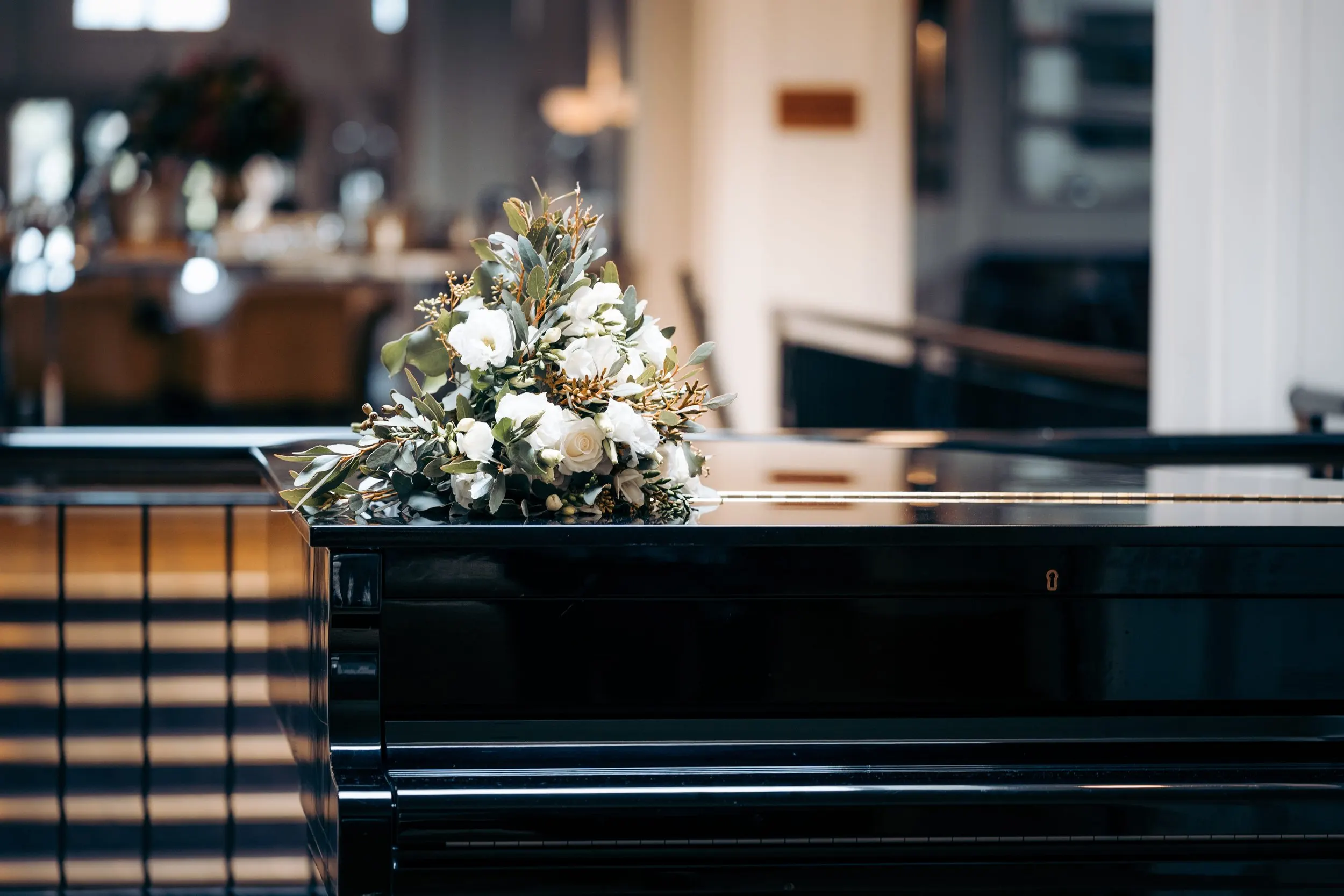 A bride's bouquet with white flowers and green leaves resting on a black piano.