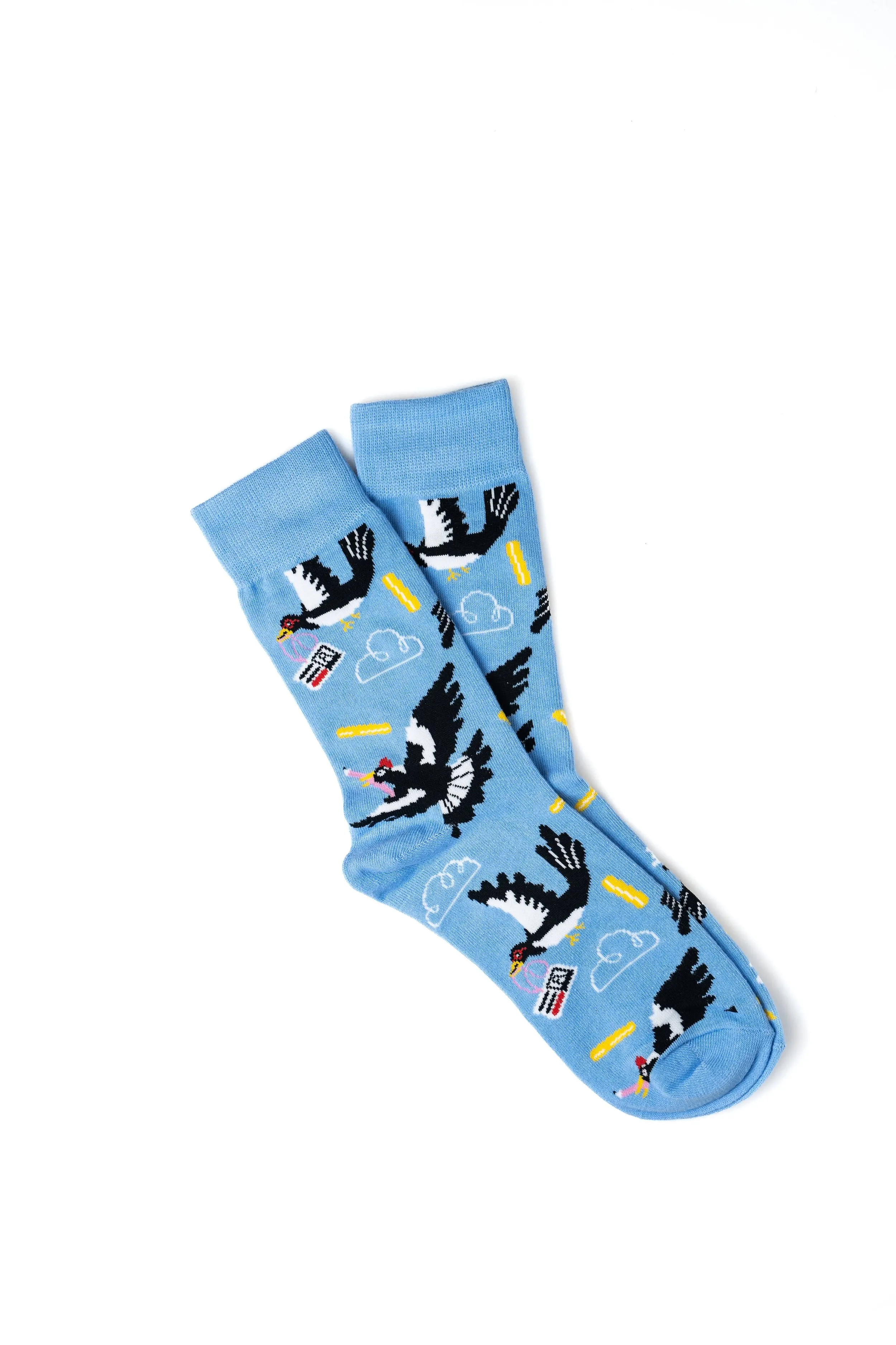 Light blue socks with pixelated black and white flying unicorns, small clouds, yellow bars, and pink and black flags on a white background.