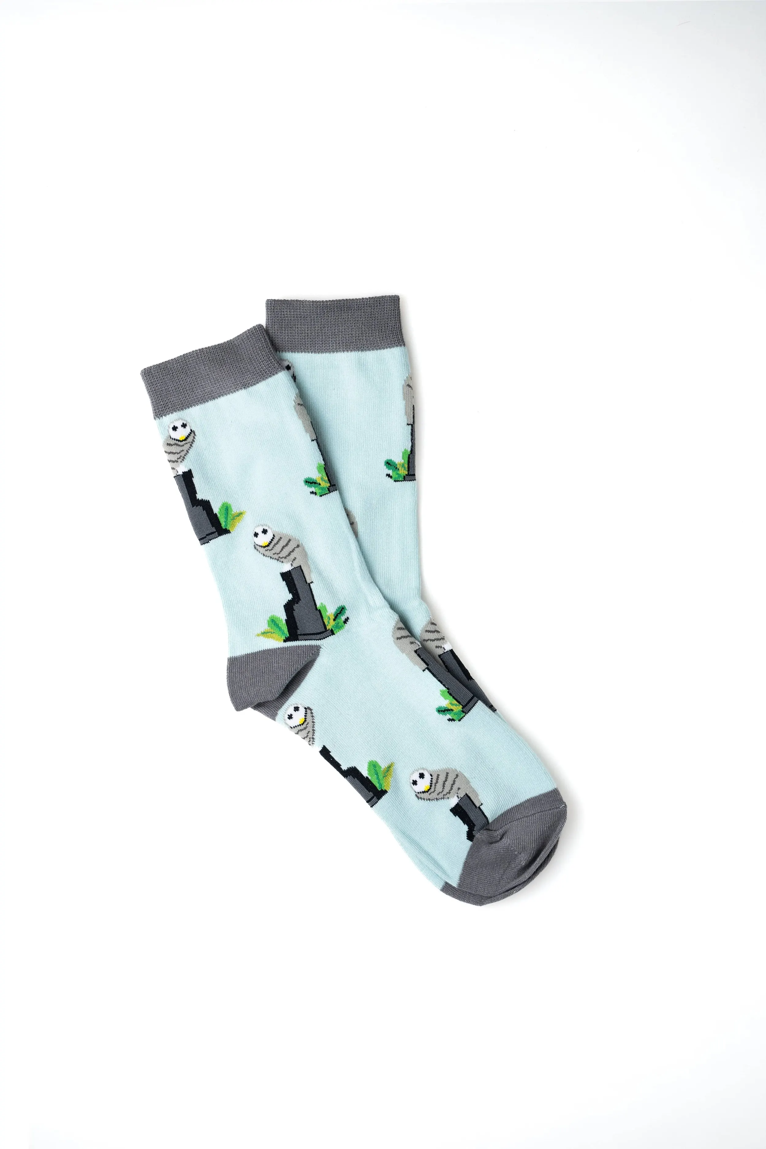 Pair of light blue socks with a design of cartoonish mummies and green plants, with gray cuffs, heels, and toes.
