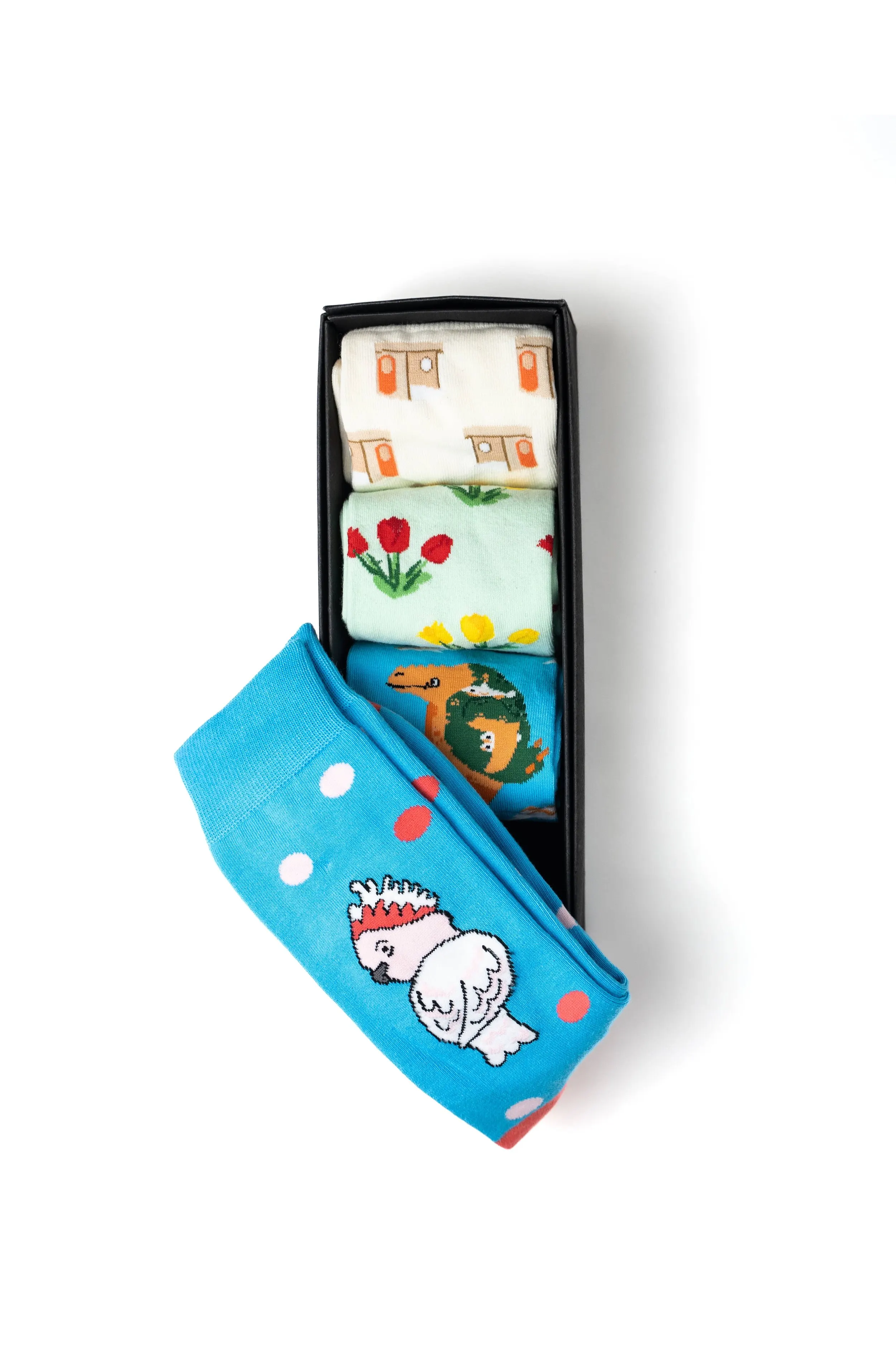 A black rectangular box with four colorful cartoon-themed socks inside, including a blue sock with a chicken design and other socks with floral and animal patterns.