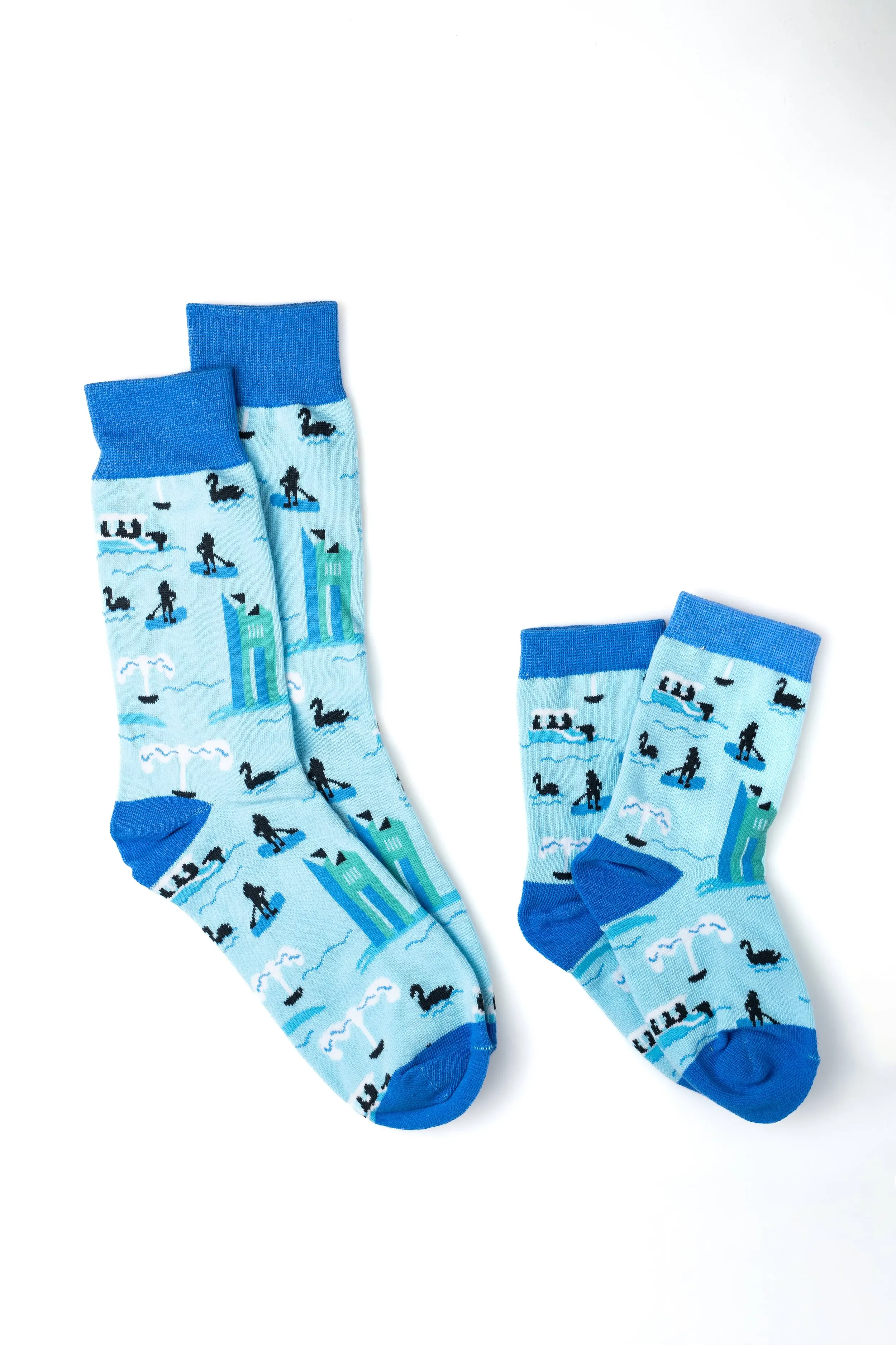 Pair of blue socks with a pattern of black swans, white clouds, and blue water, depicting a nautical scene, laid out on a white background.