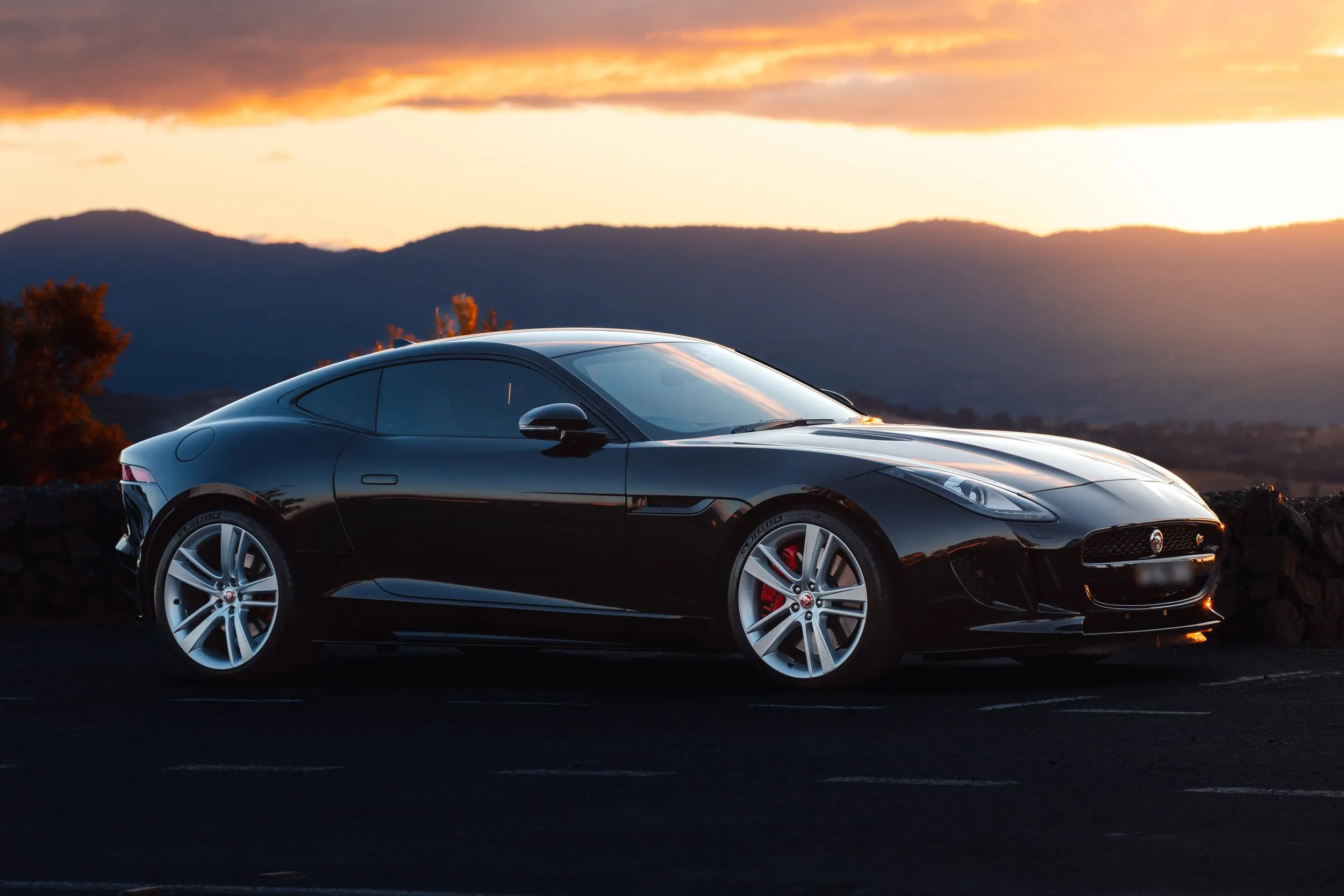 Black sports car parked on the side of a road during sunset with mountains in the background.