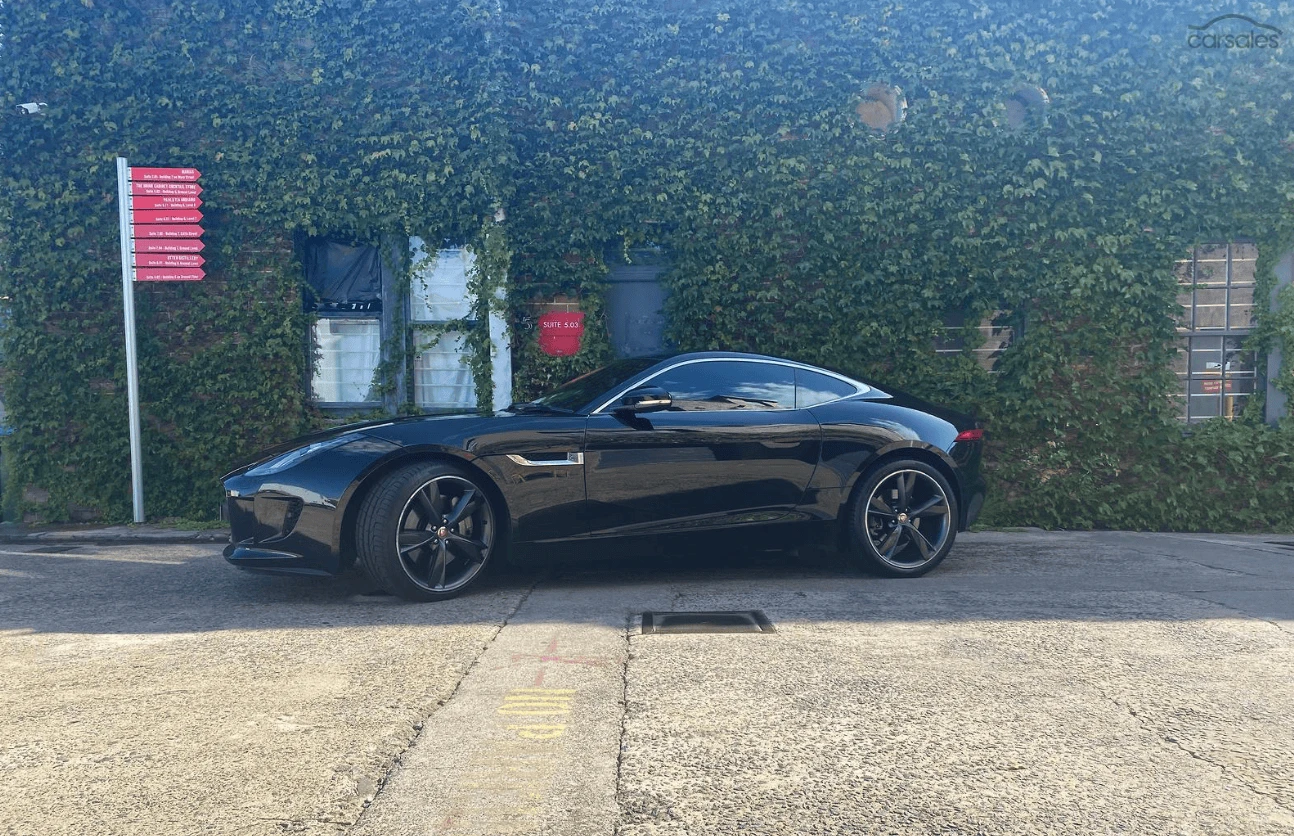 Black sports car parked on a concrete lot in front of a building covered with green ivy.