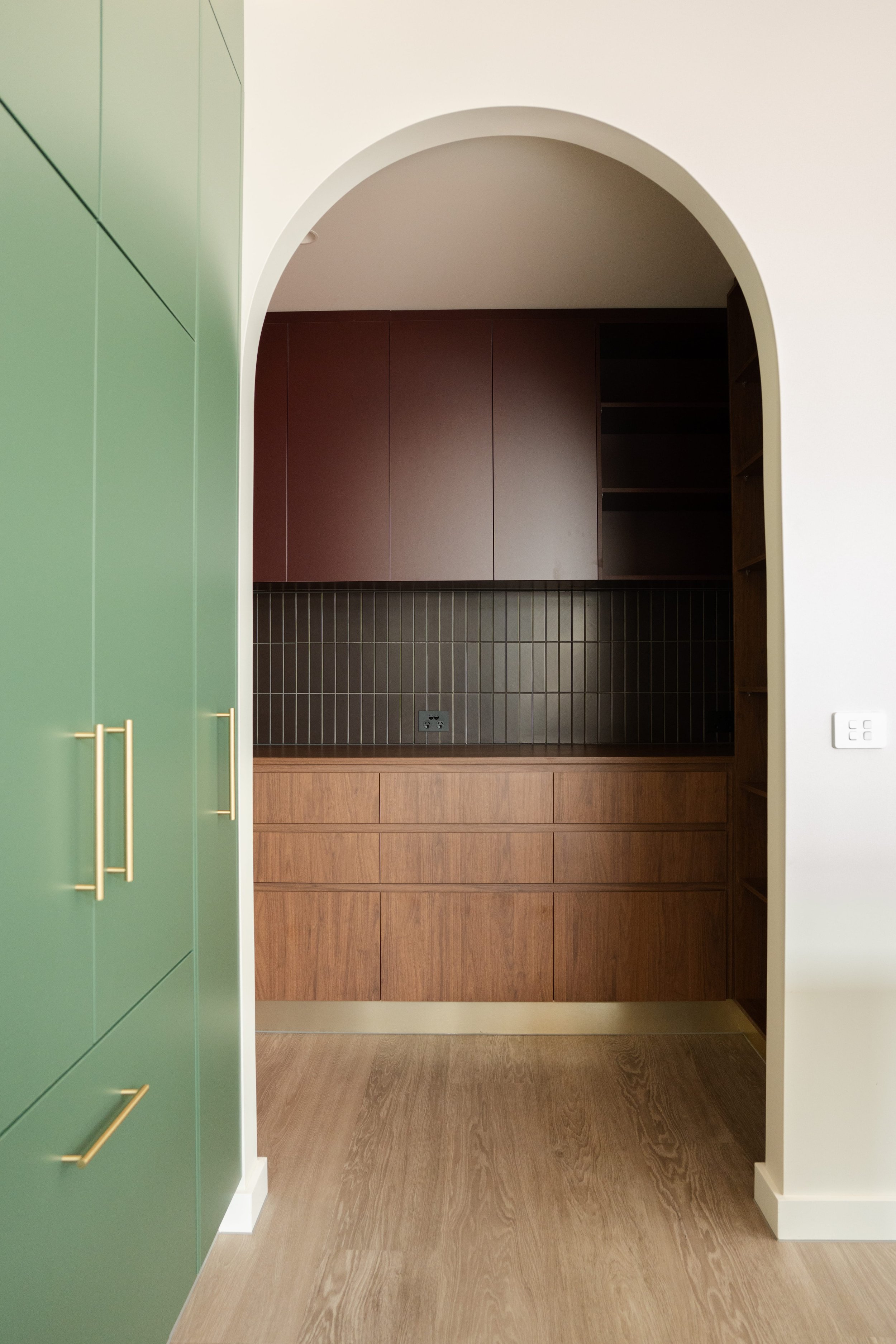 Arched doorway from a green kitchen into a timber-lined room